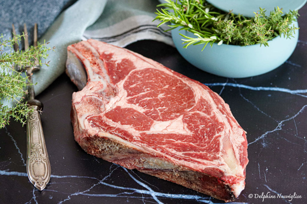 Côte de Bœuf Angus crue avec os, présentée avec romarin et thym sur ardoise