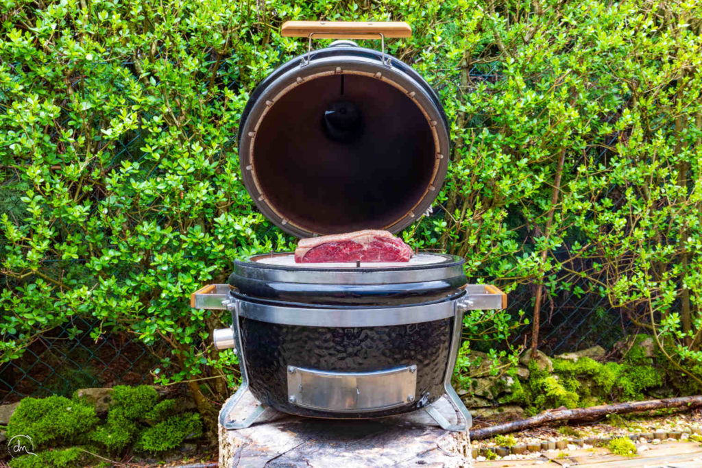 Faux-Filet Angus Argentine cru posé sur le gril d'un barbecue Kamado au jardin