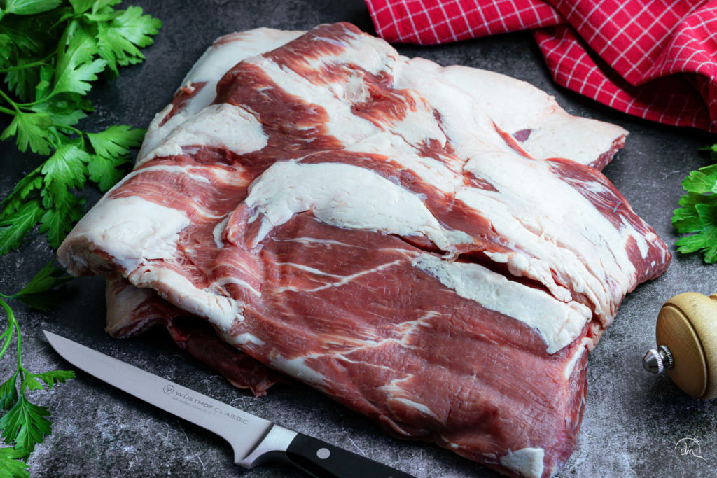 Poitrine crue de Porc Noir de Bigorre AOP sur ardoise foncée avec persil et linge à carreaux rouges