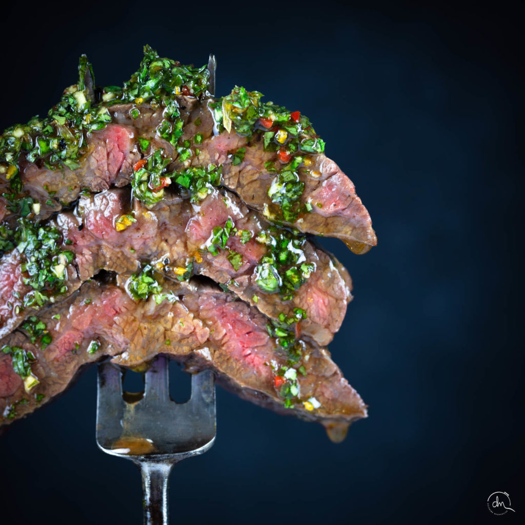 Gros plan sur la bavette d'aloyau Wagyu et sa sauce chimichurri parsemée de piment sur fond sombre