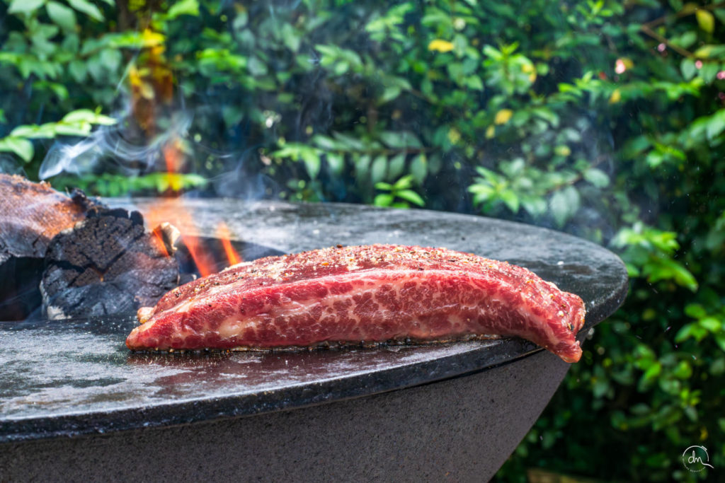 Bavette Wagyu poivrée sur le brasero plancha entourée de flammes et d'un feuillage dense