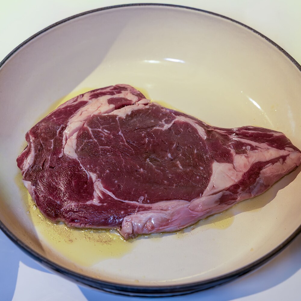 Entrecôte Fin Gras du Mézenc AOP crue, persillage apparent, déposée dans un filet d'huile d'olive avant la cuisson.