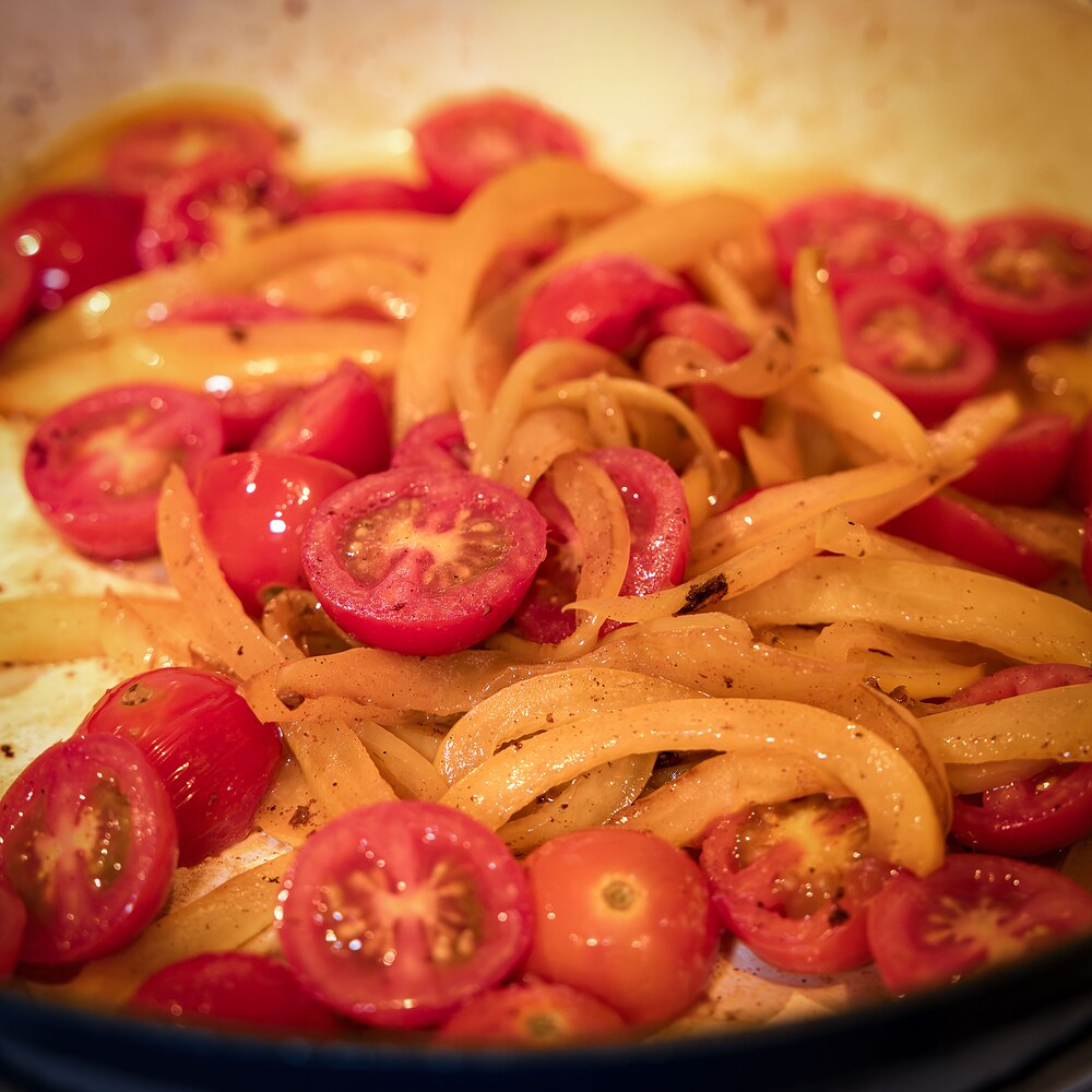 Poêlée de poivron jaune en lamelles et tomates cerises en cours de cuisson dans la poêle.